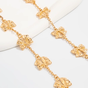 Dettaglio di ciondoli a fiocco dorati con texture radiante su una lunga collana alla moda