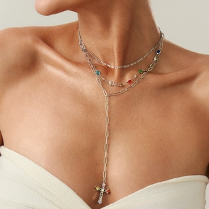 Dettaglio di gioielli a strati con cristalli multicolori e collana con ciondolo a croce