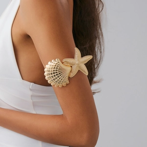 Dettaglio di un bracciale da braccio dorato con ciondoli a stella marina e conchiglia