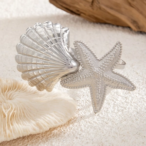 Dettaglio di portatovaglioli in argento a forma di conchiglia e stella marina su sabbia