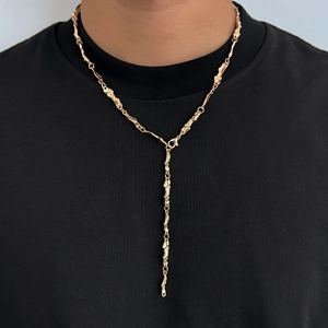 Dettaglio della collana a Y dorata con texture fusa unica su uno sfondo nero