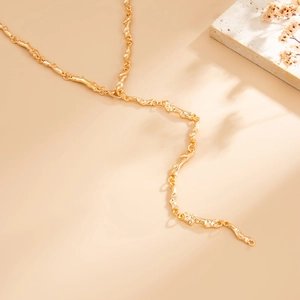 Dettaglio collana a Y dorata con trama lavica organica su sfondo di pietra naturale