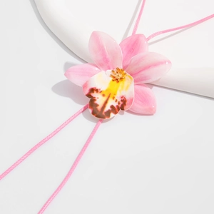 Macro detail of a 3D pink orchid flower pendant on a woven cord necklace for women