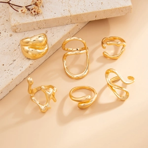 Set of six gold fluid-style rings with irregular liquid metal textures on stone steps