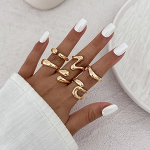 Close-up of five irregular liquid lava gold rings worn on a model's hand over white carpet