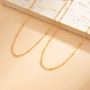 Detail of a minimalist gold waist chain with square beads on a textured stone background