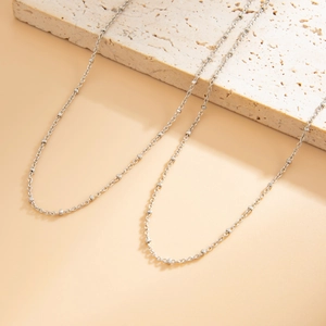 Detail view of a minimalist silver beaded chain draped over a textured beige stone stand