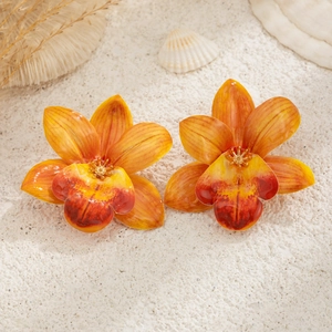 Detail shot of bright orange and yellow orchid earrings on a tropical beach sand setup