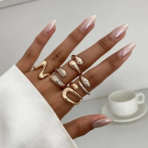 Unregelmäßiges Set goldener Metallringe mit weißen Diamanten auf Modelhand mit Kaffeetasse
