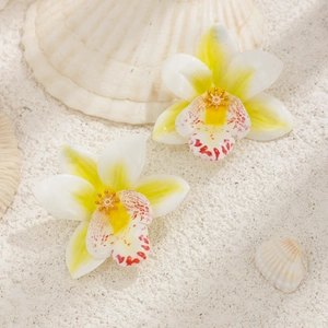 Detail of tropical orchid earrings with yellow gradient petals and gold center on sand