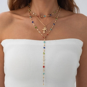 Dettaglio di collana multistrato dorata con perline colorate e ciondolo a croce