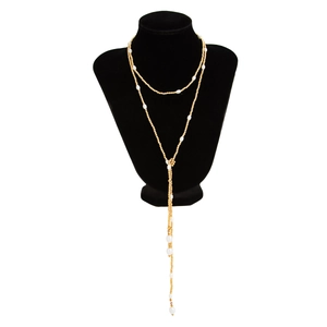 Detail van gouden Y-ketting met barokparels en schijfkwastje op een zwarte displayhals