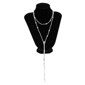 Detail van een gelaagde Y-vormige ketting met zilveren kralen en witte parels op buste