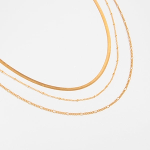Detailed view of layered gold flat snake, bead, and Figaro chains with high-gloss finish