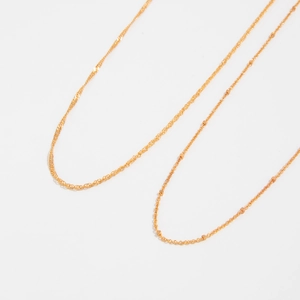 Detailed close-up of golden wavy Singapore chain and delicate satellite bead body chain