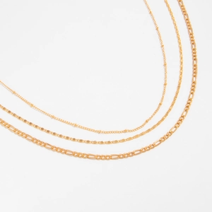 Detailed view of gold flat snake and Figaro chain necklaces set on white background