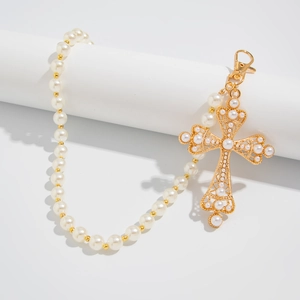 Detail of beaded trousers chain featuring white pearls and a large golden cross pendant