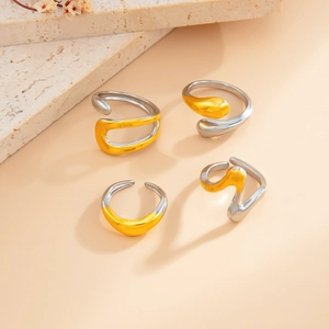 Detail of four fluid wavy open rings in gold and silver finish on stone background