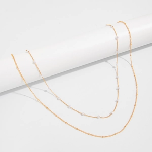 Detail view of a double-layered gold snake chain and delicate white pearl body chain