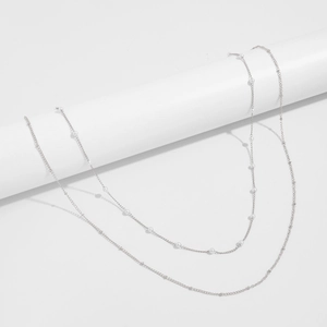 Detail shot of a minimalist silver layered chain with delicate white pearls on white background