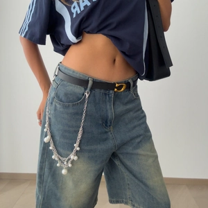 Detail of layered silver metal jeans chain with pearls and cross pendant on denim