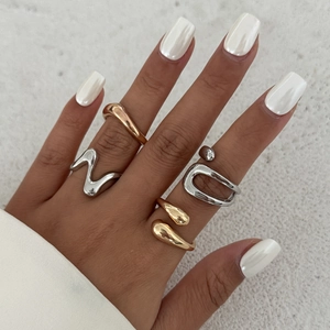 Detail shot of irregular organic gold and silver rings worn on fingers against white stone