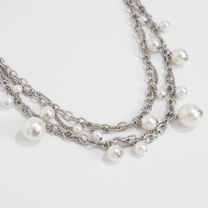 Detail of layered silver metal chains with white pearls and decorative floral petal caps