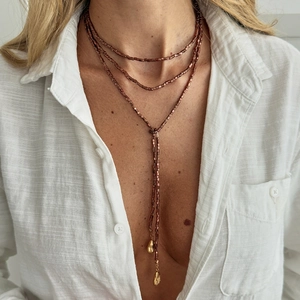 Detail van een gelaagde kralenketting met gouden druppelhangers op wit linnen shirt