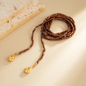 Detail van lange kralenketting met gouden hangers en kubusvormige kralen op stenen ondergrond