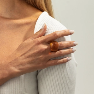 Detail eines bernsteinfarbenen Harzrings mit abgerundetem Design am Finger eines Models