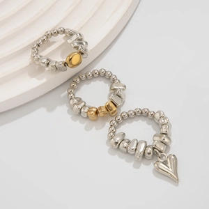 Dettaglio del set di anelli con perle metalliche elastiche e ciondoli a cuore dorato