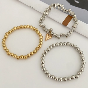 Dettaglio di tre braccialetti di perline in oro e argento con ciondolo a cuore unico