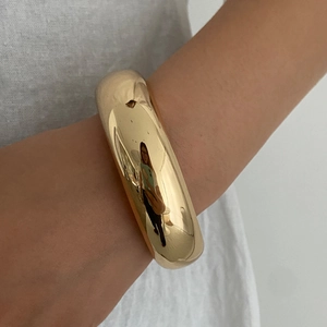 Close-up of a wide polished gold cuff bracelet worn on wrist with minimalist design