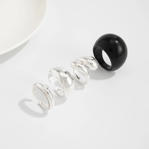 Detail van vierdelige set met zilveren metalen ringen en grote zwarte hars bolvormige ring