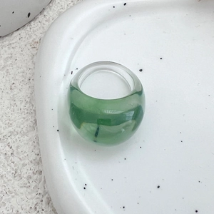 Nahaufnahme eines transparenten grünen Harzrings mit breitem Bogen auf einer Keramikschale