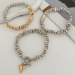 Dettaglio di braccialetti minimalisti con perline d'argento e ciondolo a cuore dorato