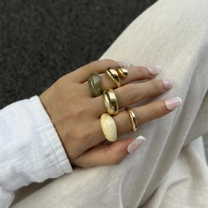 Detail van 5-delige ringenset met goud metaal, groene hars en een crèmekleurige druppelring