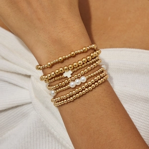 Détail de bracelets à perles dorées multicouches avec croix blanche et perles au poignet