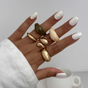 Detailopname van gouden metalen ringen en marmeren harsringen aan de vingers van model