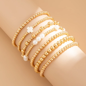 Détail d'un ensemble de 7 bracelets bohèmes dorés avec perles blanches et croix acrylique