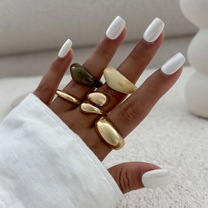 Close-up van minimalistische gouden en hars ringen in groen en crème aan een hand