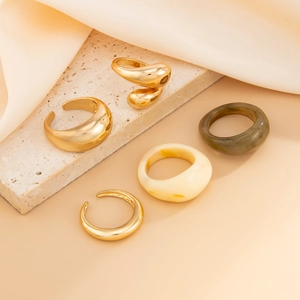Detail van 5 grove ringen van metaal en hars in goud, crème en olijfgroen