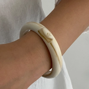 Detailed view of an amber acrylic wide bangle with marble texture worn by a model