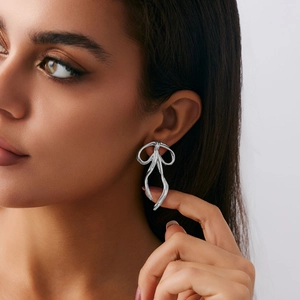 Silver bow-shaped ribbon earrings with polished metallic finish worn by a model