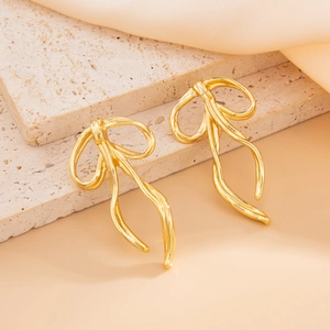 Detailed shot of golden liquid metal bow earrings on a textured stone surface