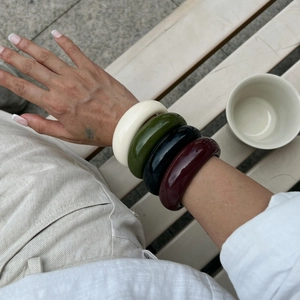 Close-up of four thick resin bangles in cream, green, black and burgundy on a wrist