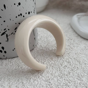 Dettaglio di un anello bombato minimalista in resina color crema con finitura lucida