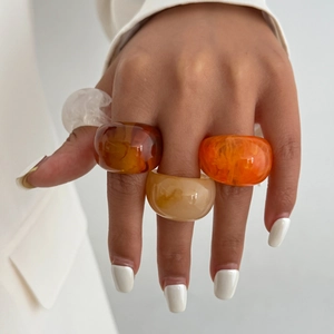 Nahaufnahme klobiger Harzringe in Bernstein und Creme an der Hand eines Models