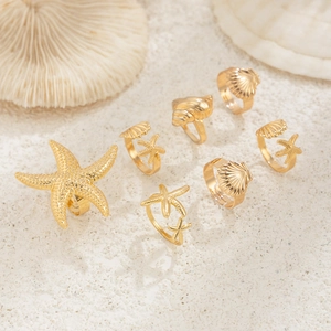 Makroaufnahme von goldenen Seestern- und Muschelringen auf weißem Sand mit Korallen