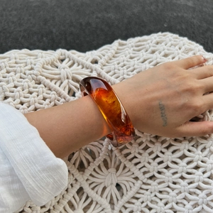 Close-up of a chunky amber resin bangle with transparent texture on a model's wrist